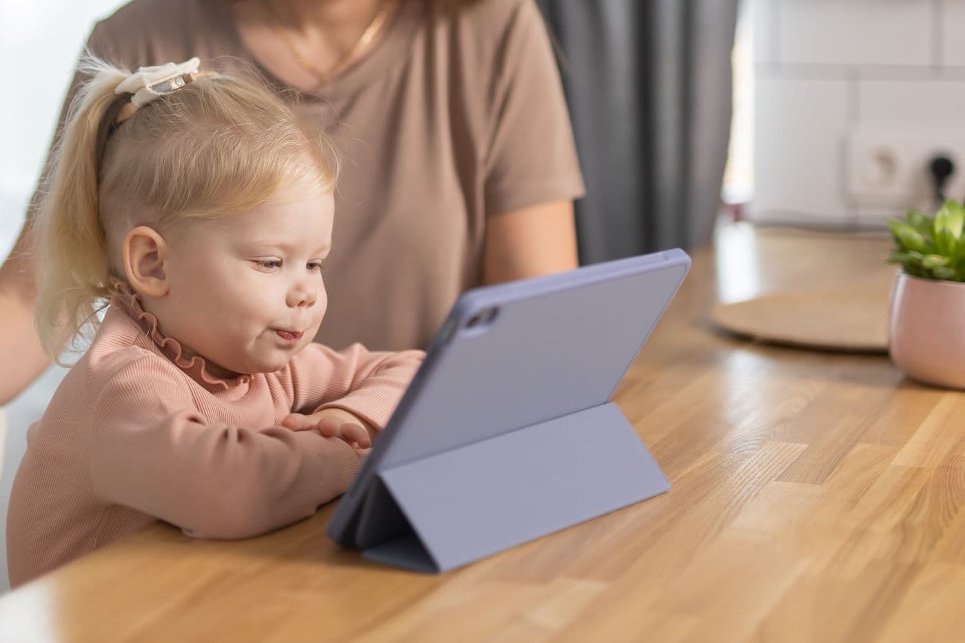 A toddler looks at an iPad while her mother watches